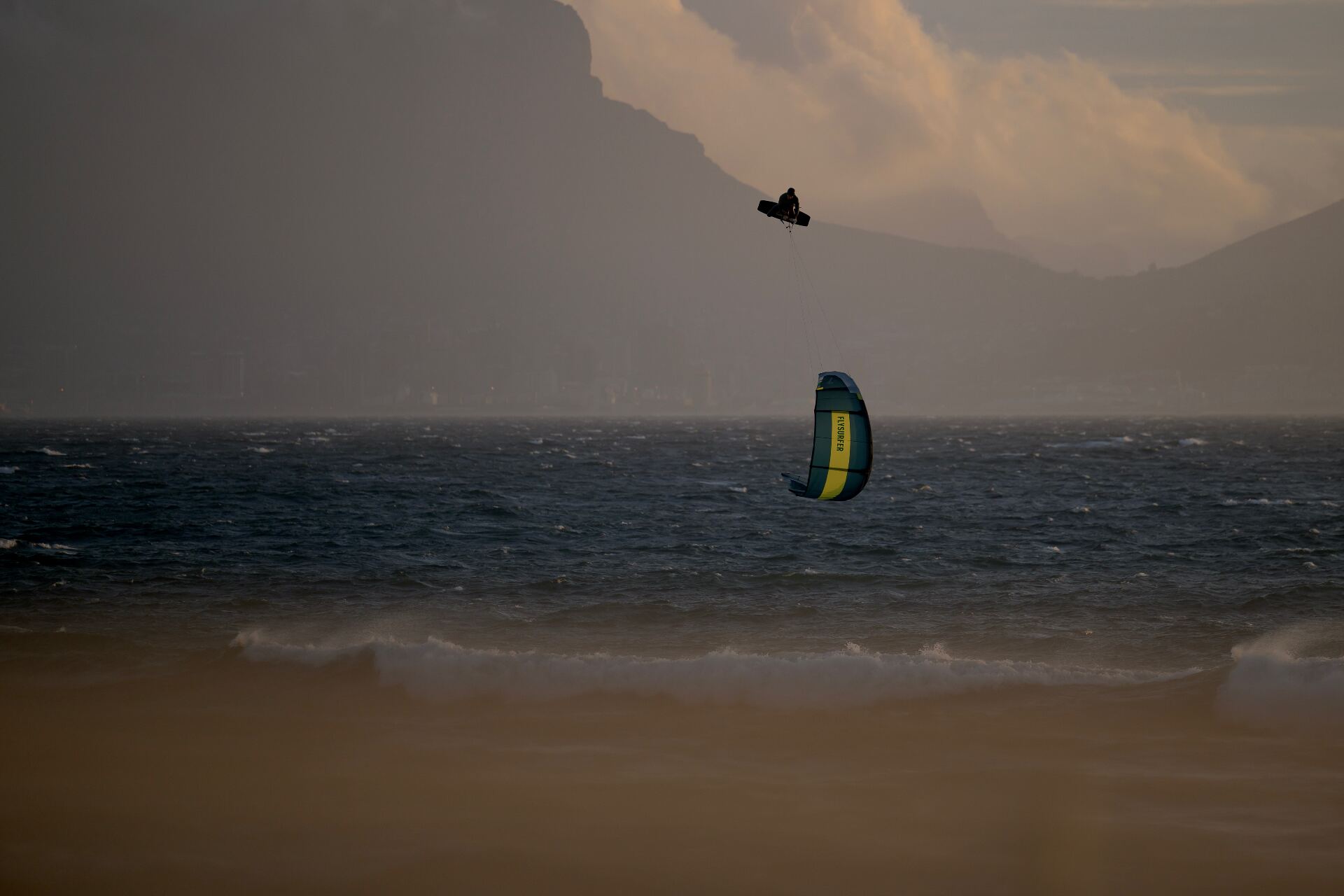 Silhouette of a kitesurfer launched high above a stormy ocean at dusk in front of a mountain range
